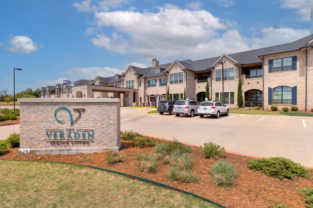 Exterior view of The Veraden Senior Living showing brick building, sign, and parked cars.