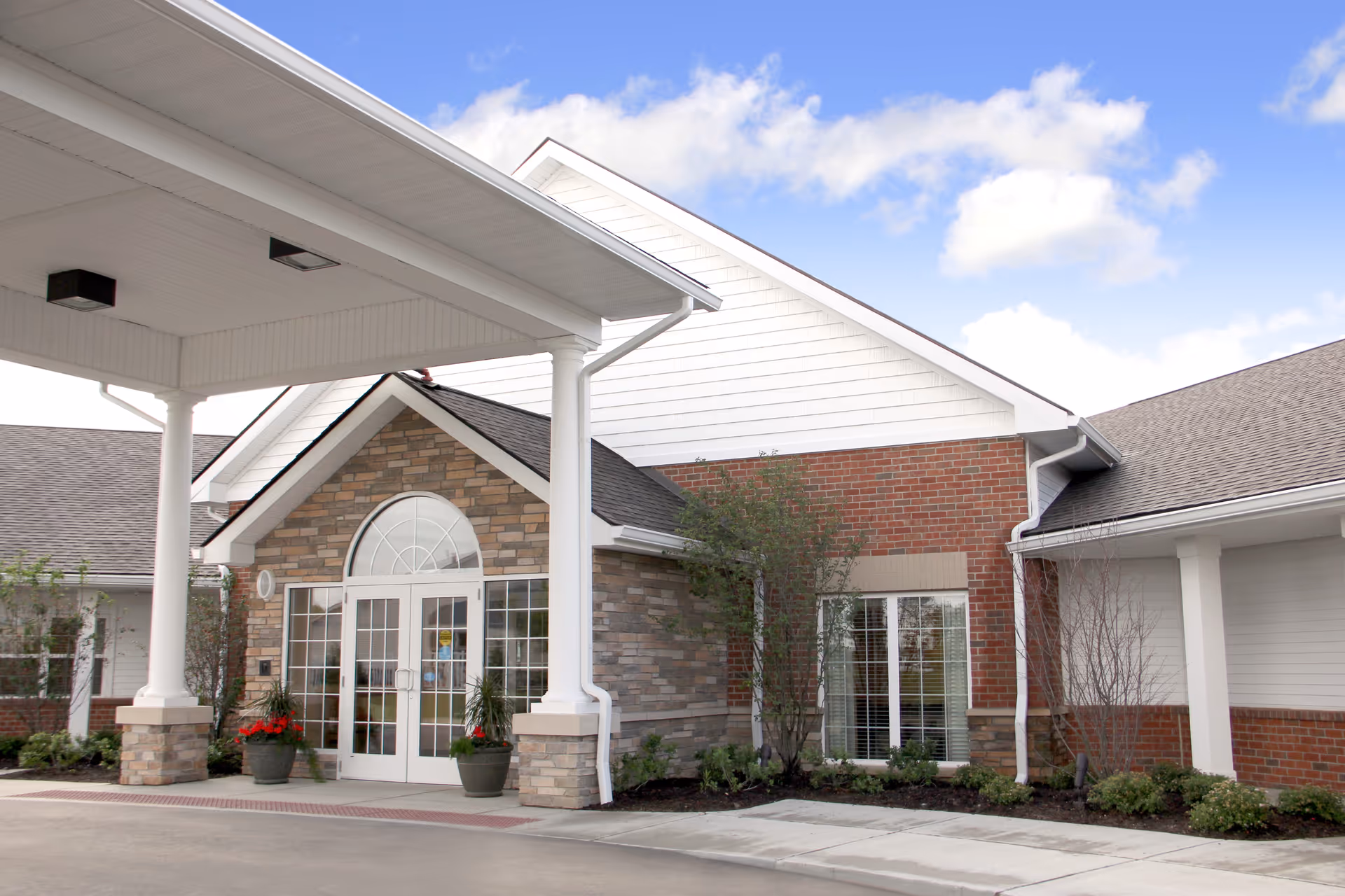 Covered main entrance with white columns, double glass doors, and a stone-and-brick facade under a blue sky.