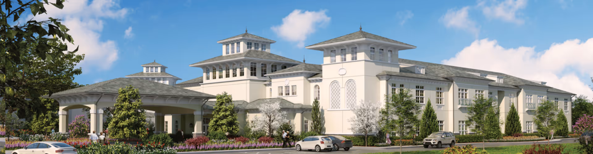 Exterior view of a large, elegant senior living facility building with multiple windows, a covered entrance, and landscaped greenery including trees and bushes under a blue sky with some clouds.
