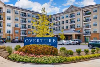 Exterior front of a multi-story apartment-style senior living building with a landscaped entrance and a prominent 'OVERTURE' sign.