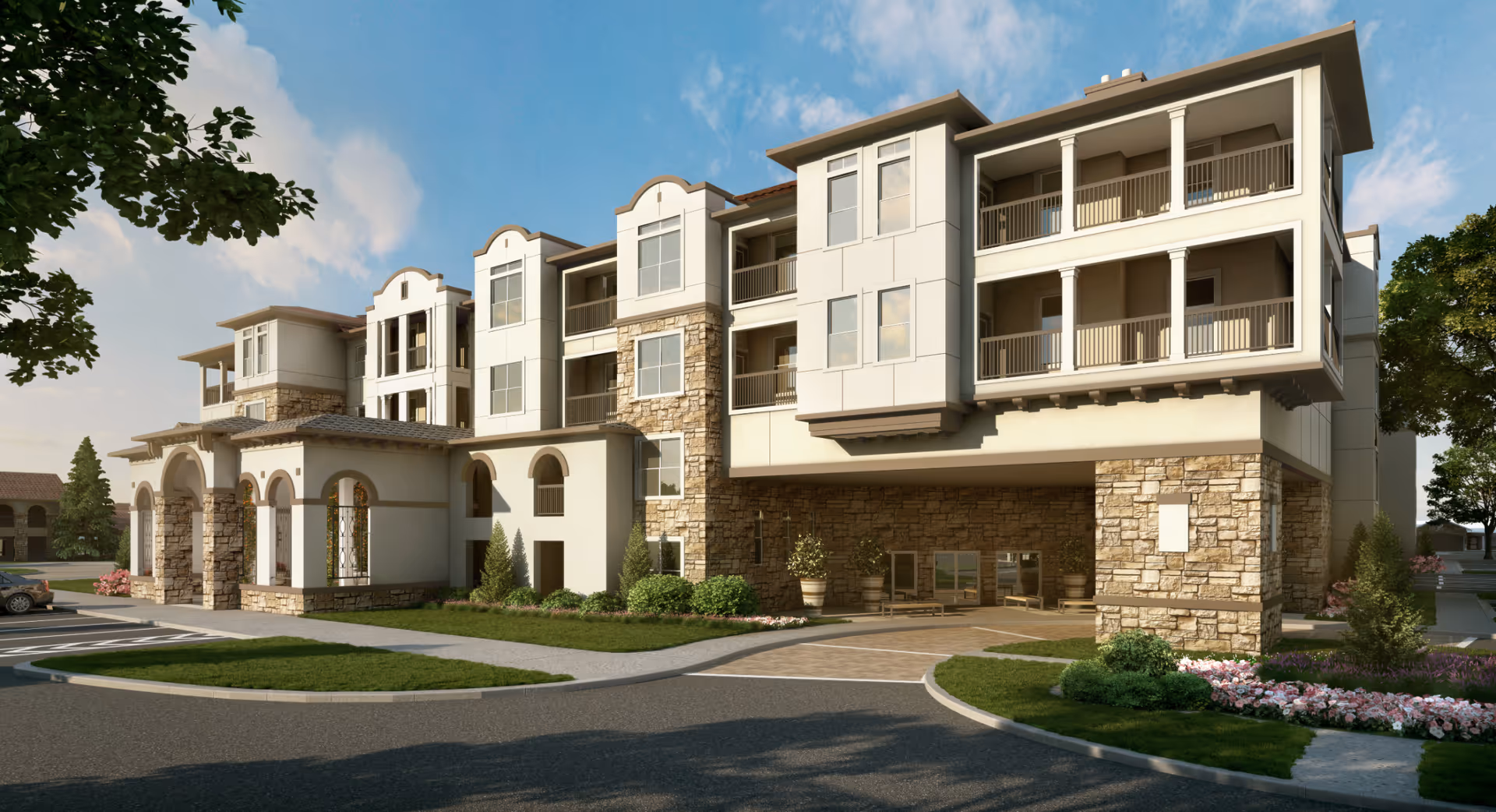 Exterior view of a modern senior living facility building with stone and stucco facade, multiple balconies, arched entryways, landscaped greenery, and a driveway under a clear blue sky.