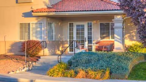 Front exterior of a senior living facility with a covered entrance and seating.