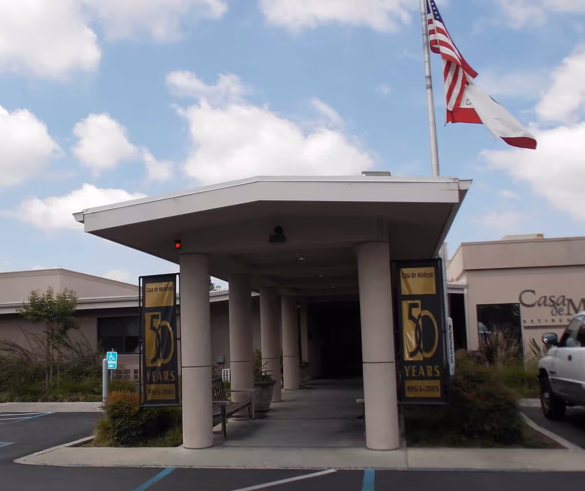Covered entrance with columns, banners, and an American flag at the front of the Casa de Modesto building.
