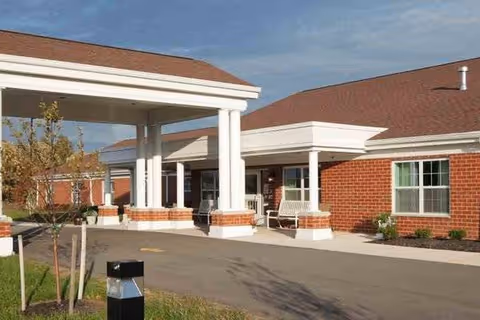 Front exterior of Elderwood at Wheatfield with brick building, white columns, and covered entrance.