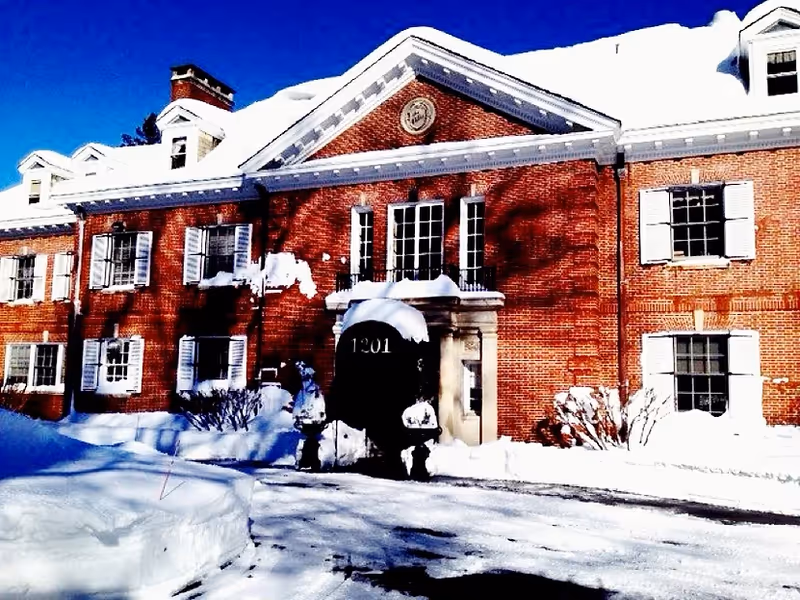 Snow-covered red brick building with white shutters and a central arched entrance under a clear blue sky.