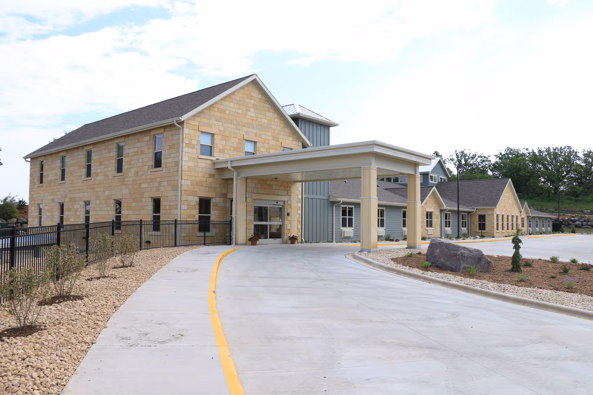 Front exterior of a memory care building with a covered drive-up entrance, stone facade and paved circular driveway.