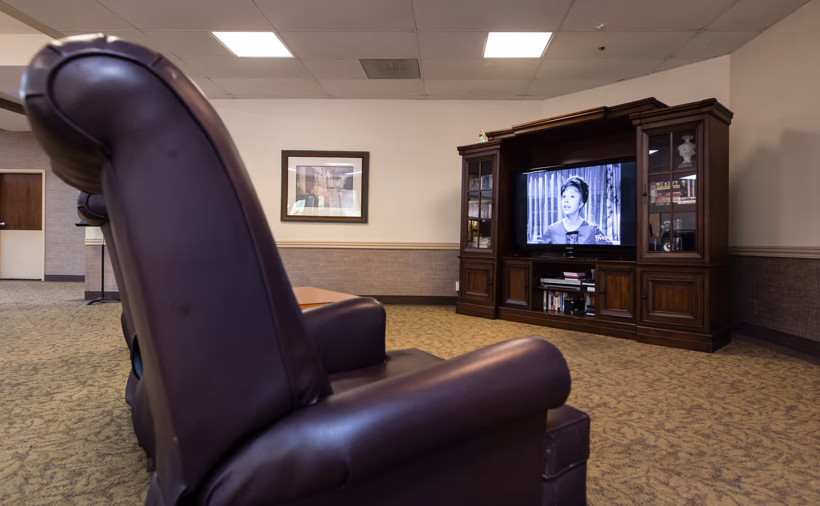 A lounge area with leather recliner chairs facing a wooden entertainment center with a television playing a black-and-white program.