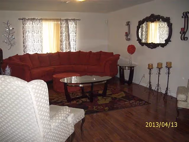 Cozy living room with a red sectional sofa, glass coffee table, patterned rug, and wall mirror.