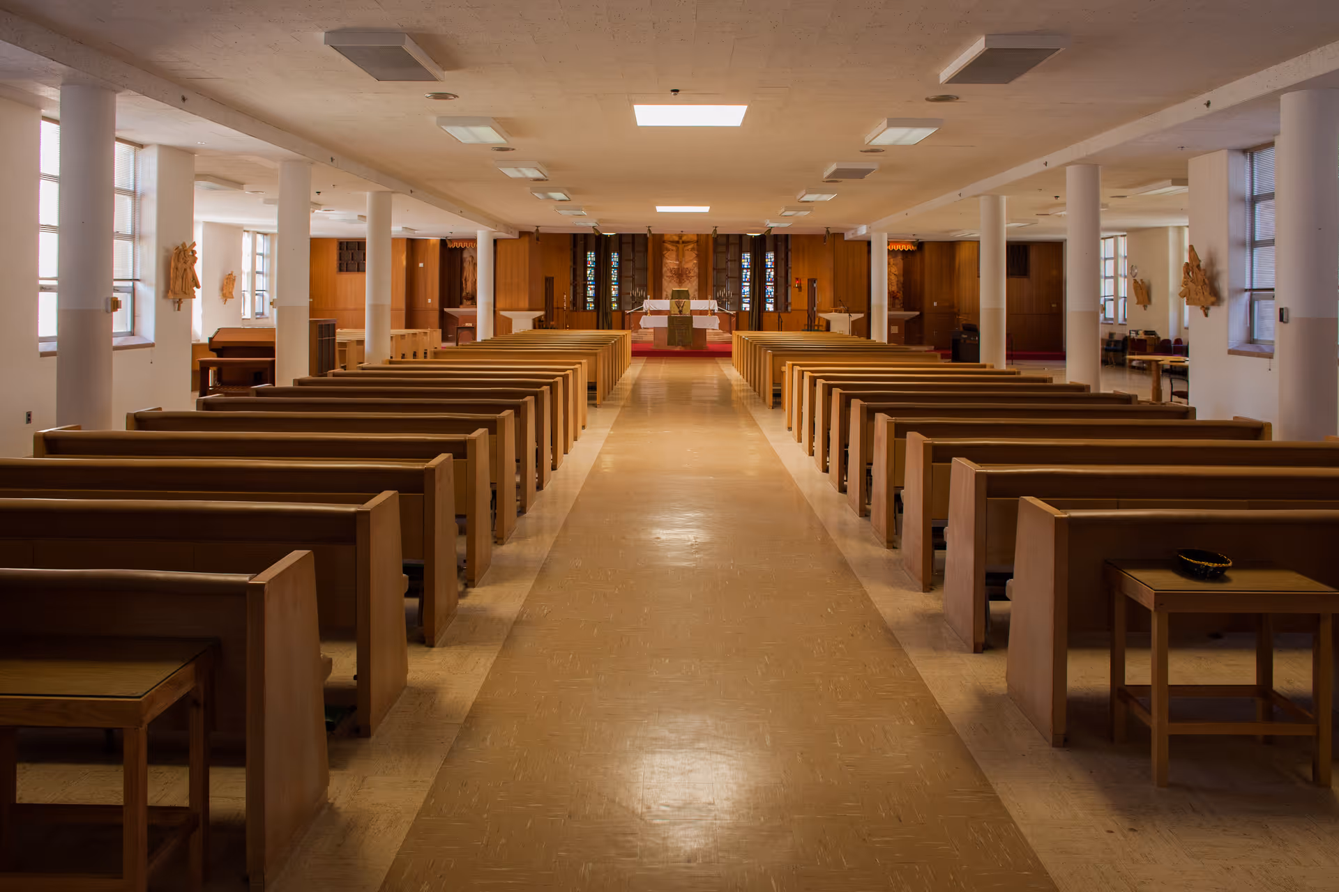 Interior view down the center aisle of a chapel or worship space with wooden pews and an altar at the far end.
