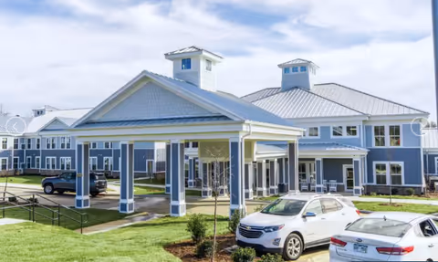 Front exterior of the Arbor Ridge at Huntersville building with a covered porte-cochere entrance, lawn and parked cars.