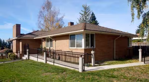 Single story brick senior living home with a fenced walkway and grassy lawn.