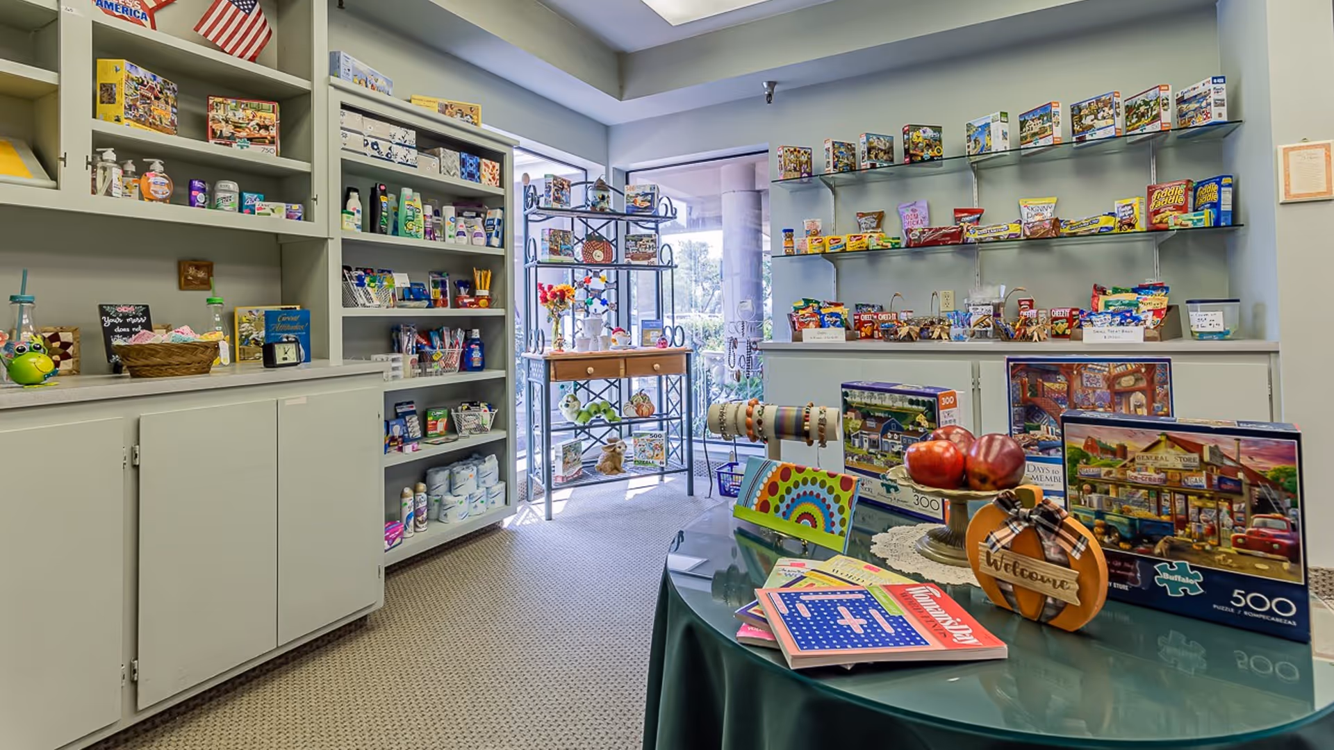 Small on-site shop in a senior living facility with shelves of snacks, puzzles, and personal items and a display table in the foreground.