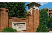 Brick entrance sign for Richland Place with greenery and a gated fence in the background under a clear blue sky.