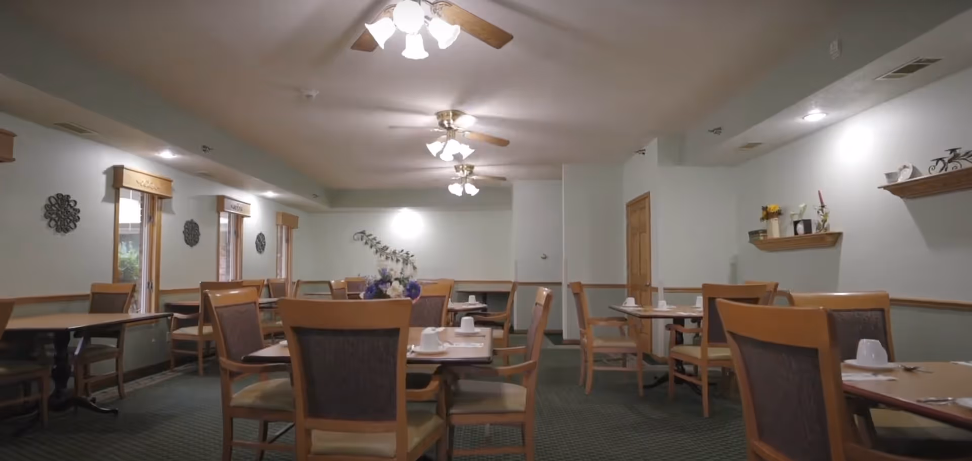 Communal dining room with wooden tables and chairs, ceiling fans, and place settings.