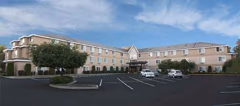 A beige, multi-wing senior living facility exterior with a parking lot and trees.