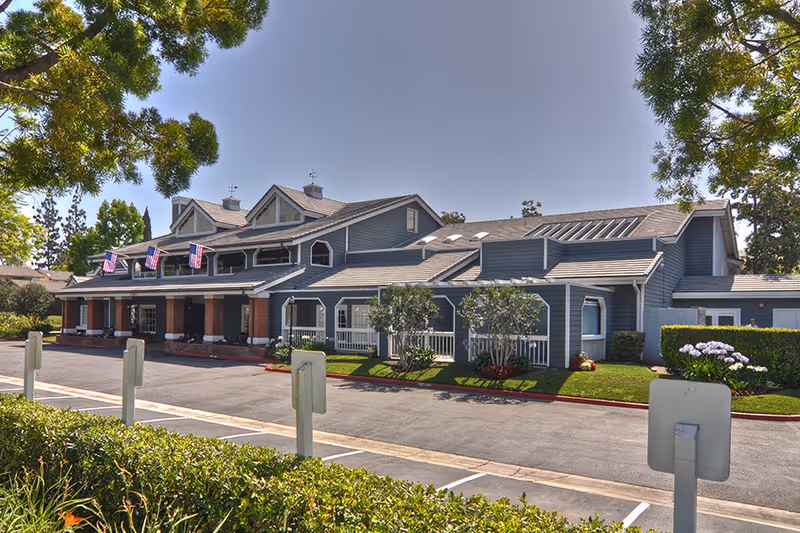 Exterior view of a blue senior living facility with a parking lot and manicured landscaping.