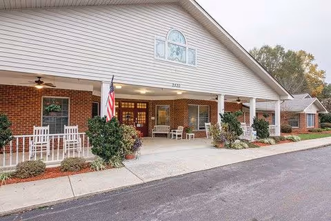 Senior living facility entrance with a covered porch, white columns, benches, and an American flag.