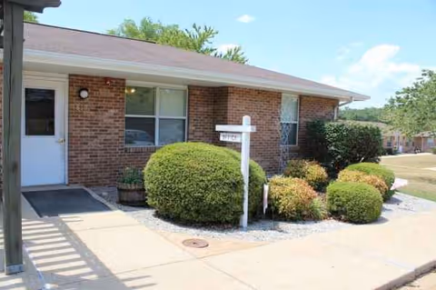Brick exterior of Summit Terrace facility with front door, windows, and trimmed shrubs.