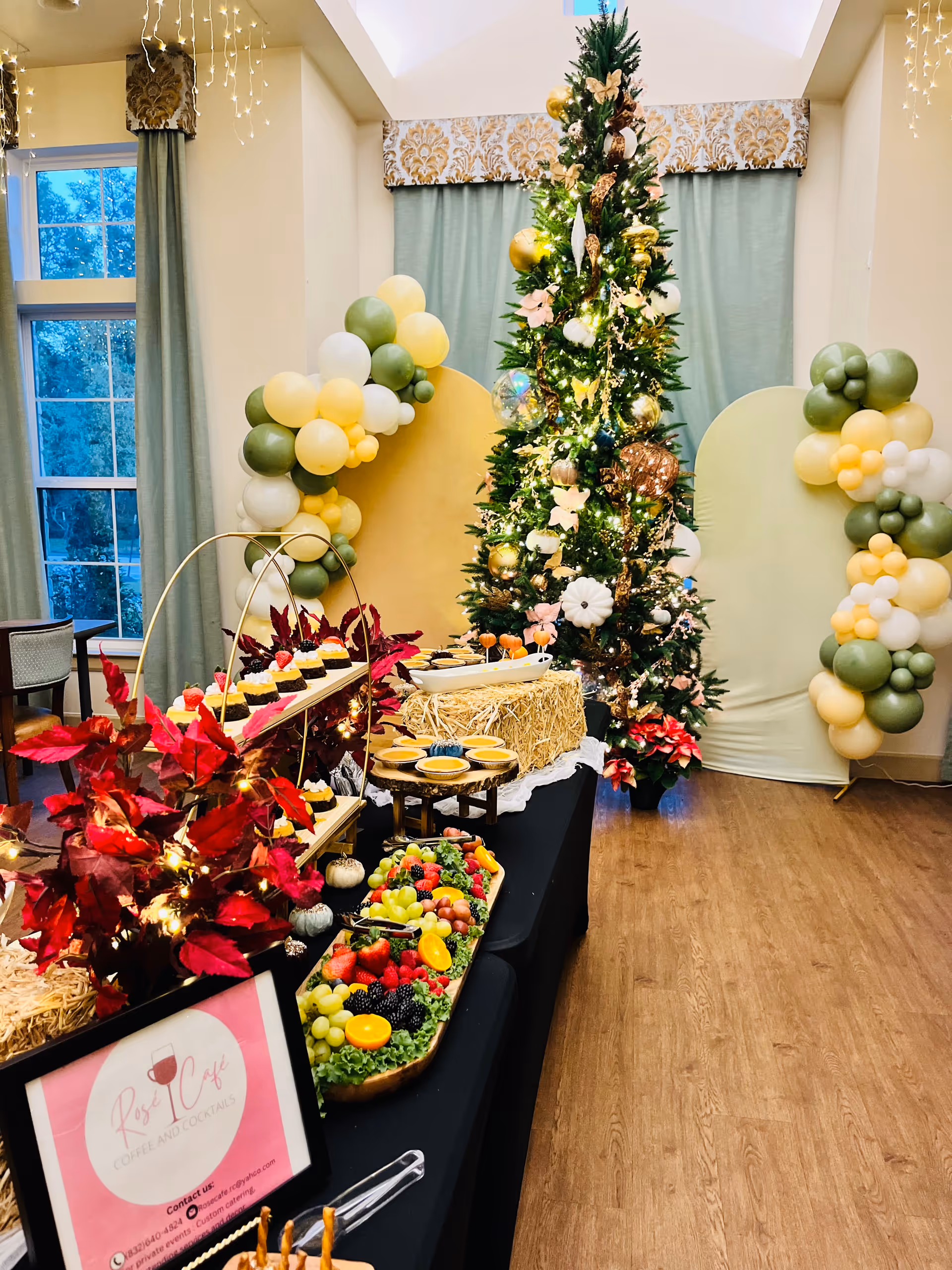 Festively decorated dining area with a Christmas tree, balloon arches, and a buffet table of fruits and desserts.