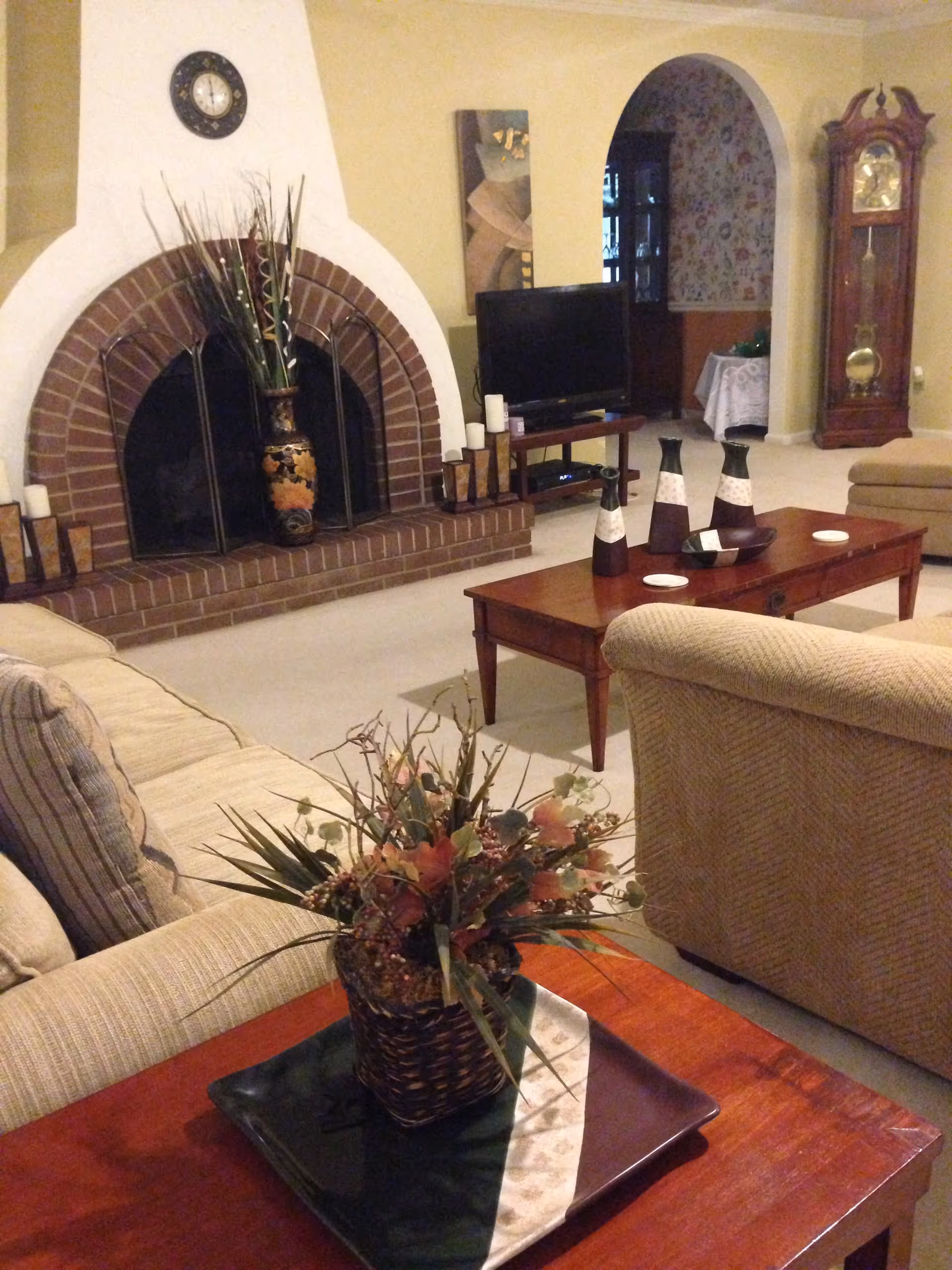 Cozy living room with an arched brick fireplace, television, coffee table, and a floral centerpiece on an end table.