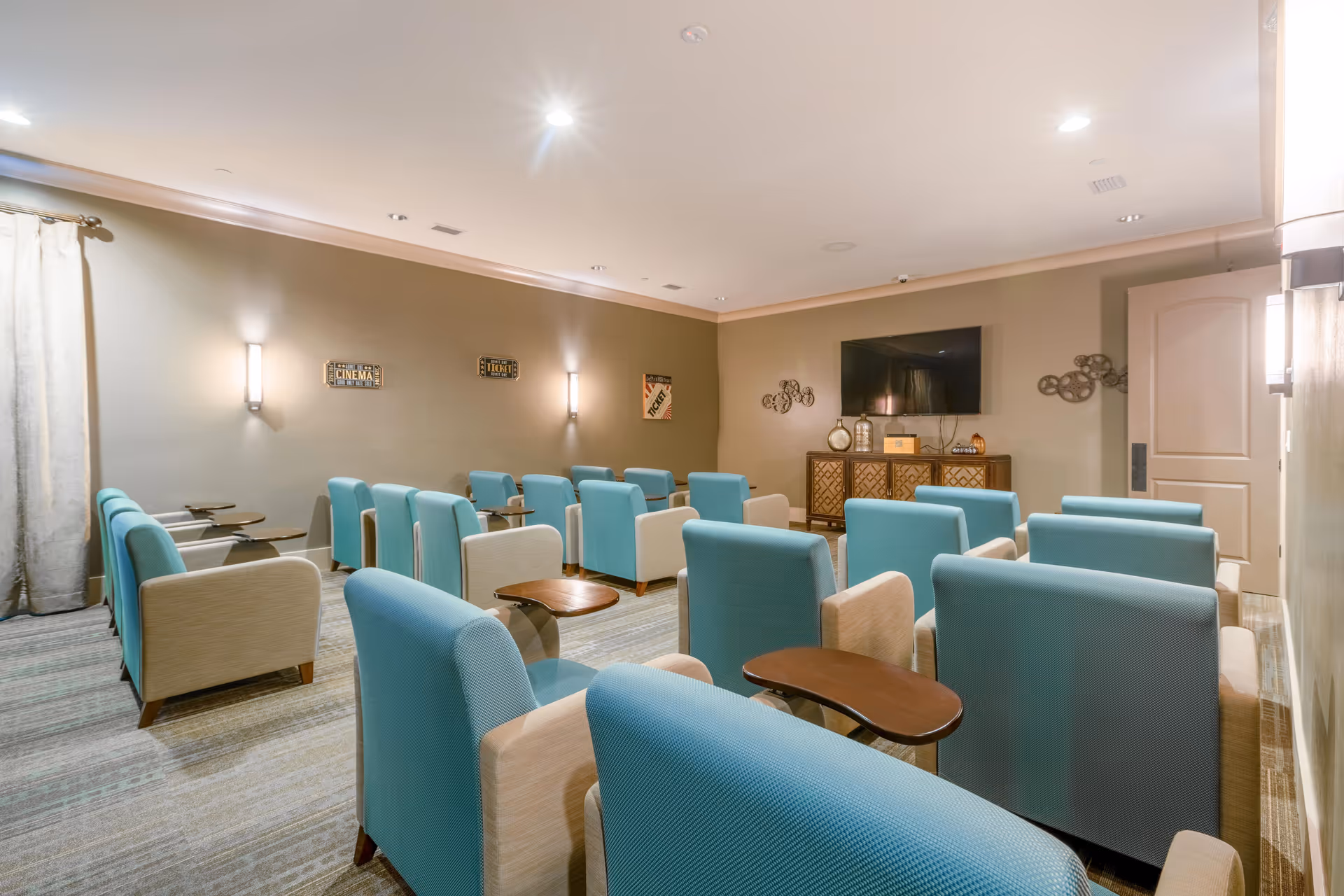 A small screening room with rows of turquoise and beige armchairs facing a wall-mounted TV and media console.