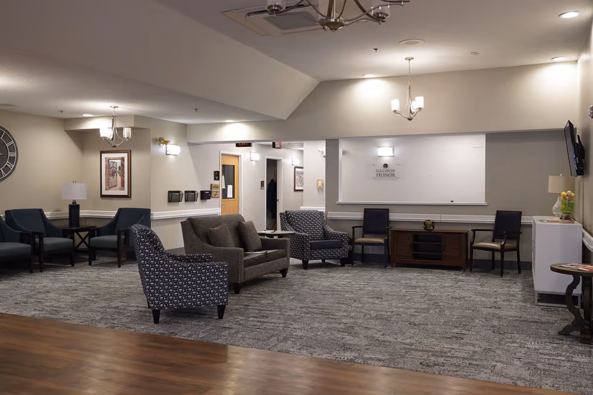 Furnished senior living community common lounge with armchairs, side tables, and overhead lighting.