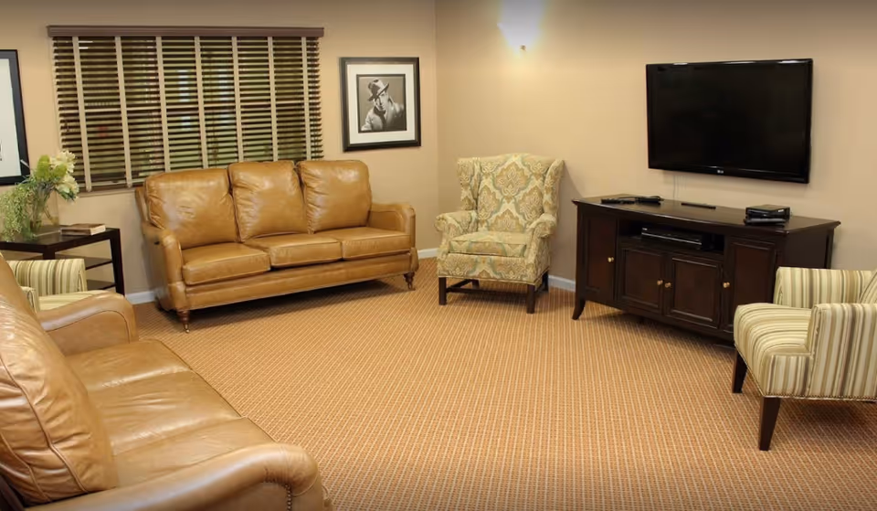 Cozy living room with leather sofas, upholstered chairs, a wall-mounted TV and a wooden media console.