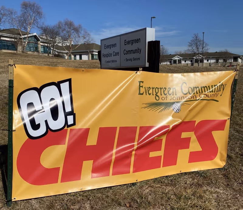 A large yellow "Go Chiefs" banner on a lawn in front of an Evergreen Community senior living sign and buildings.