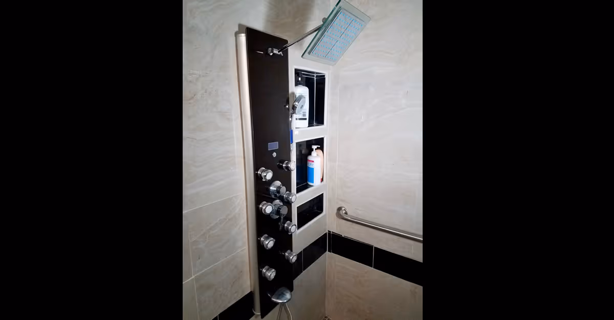 Modern shower panel with multiple controls and a rainfall showerhead, built-in wall niches with toiletries, and a grab bar on tiled walls.