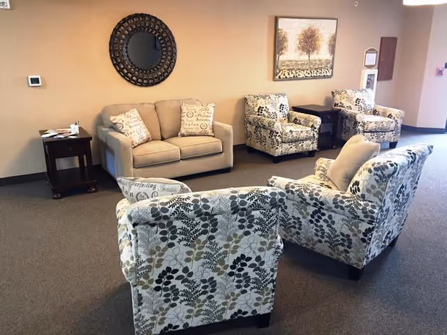 A communal seating area with a loveseat, patterned armchairs, side tables, a decorative mirror and wall art.