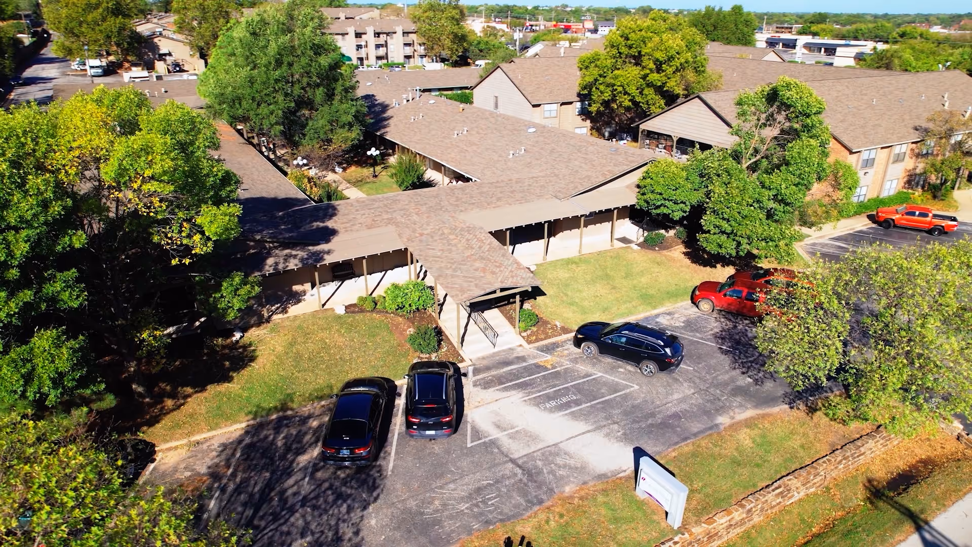 Aerial view of Leisure Village Health Care buildings with a parking lot, several parked cars, and surrounding trees and lawns.