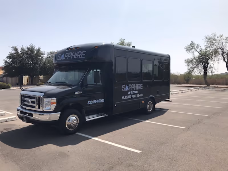 A black shuttle bus labeled 'SAPPHIRE of Tucson Nursing and Rehab' parked in an empty parking lot.