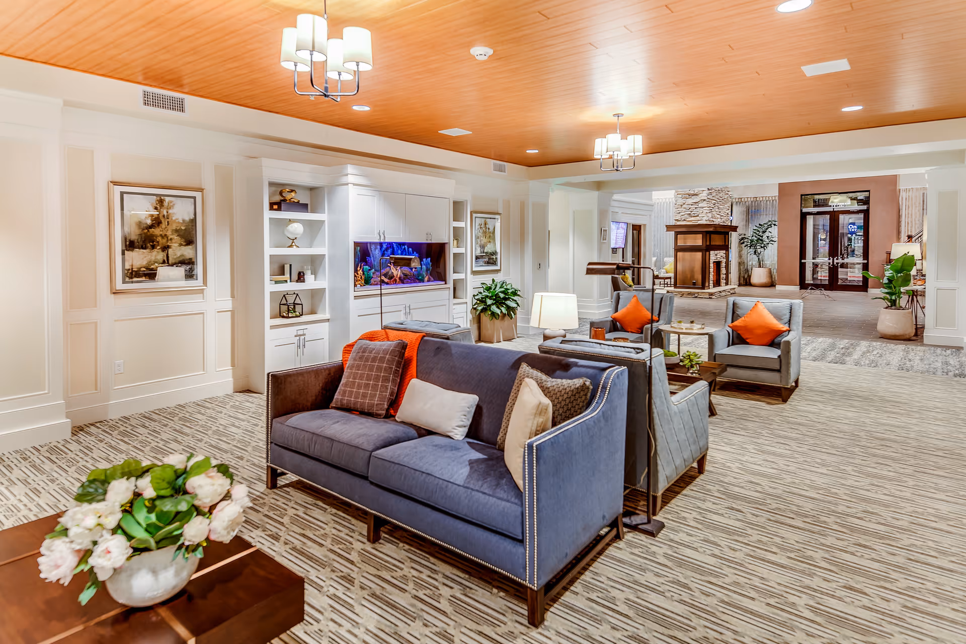 Spacious, well-lit common lounge with sofas and armchairs, a built-in aquarium, and decorative plants and lamps.