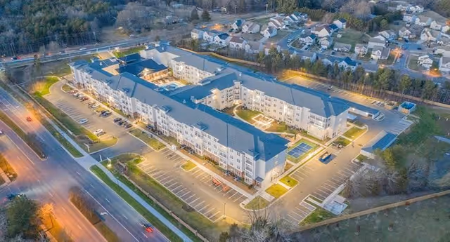 Aerial view of Sage Highland Creek senior living facility at dusk, showing a large multi-story building with surrounding parking lots and nearby residential houses.