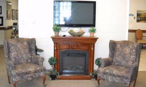 Two upholstered armchairs sit beside a wooden fireplace with a mounted TV above.