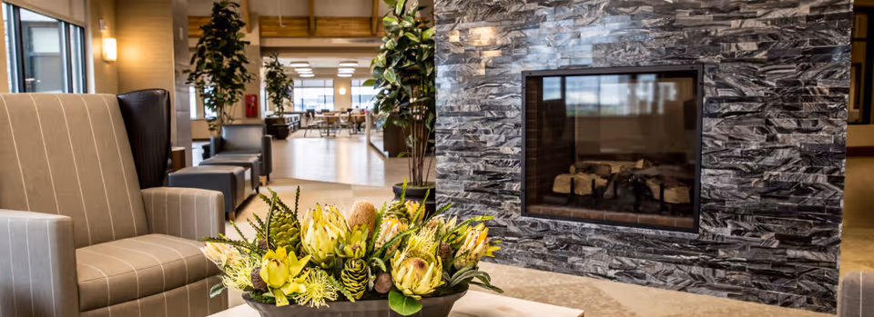 Comfortable lounge area with armchairs, a coffee table holding a floral arrangement, and a stone fireplace in the background.