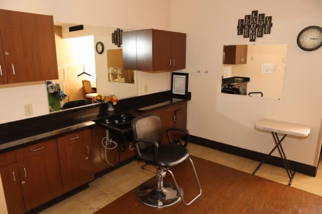 Small salon-style room with a barber chair, shampoo sink, mirrors, and wooden cabinetry.