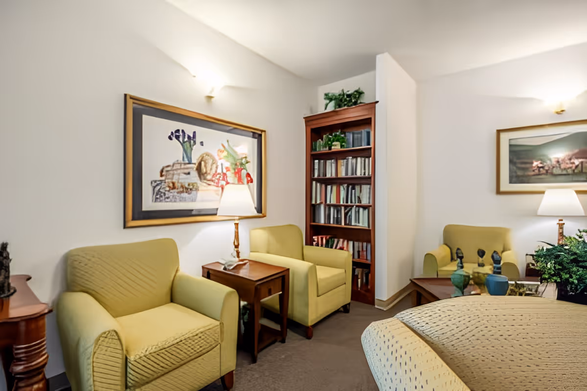 Cozy sitting area with yellow armchairs, side tables and lamps, a bookshelf, and framed artwork on the walls.