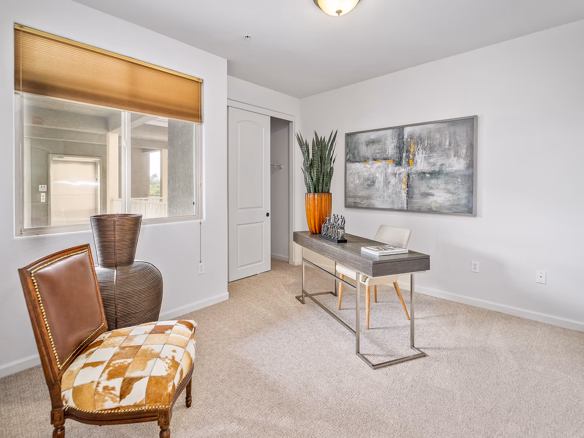 Bright furnished interior room with a desk, chairs, decorative plant and abstract artwork on the wall.