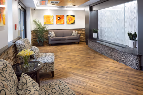 Cozy lobby seating area with patterned chairs, sofa, plants, wall art, and a water feature.