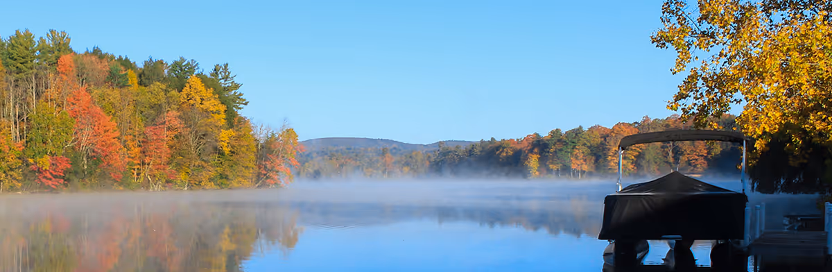 Calm autumn lake with colorful trees reflected in the water and a covered boat tied to a dock on the right.