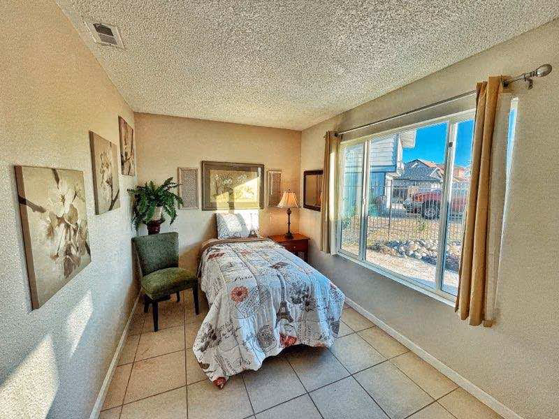Small bright bedroom with a single bed, nightstand and lamp beside a large window.
