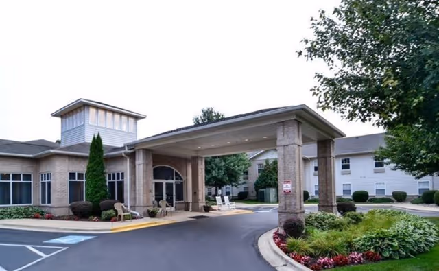 Entrance of Cedarhurst Senior Living of Edison Lakes showing a covered drop-off area with columns, surrounded by landscaped greenery and a paved driveway.