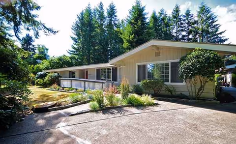 Single-story senior living facility exterior with a driveway, landscaping, and surrounding trees.