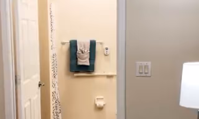 View into a bathroom showing a towel rack with folded towels, a shower curtain, and a toilet paper holder.