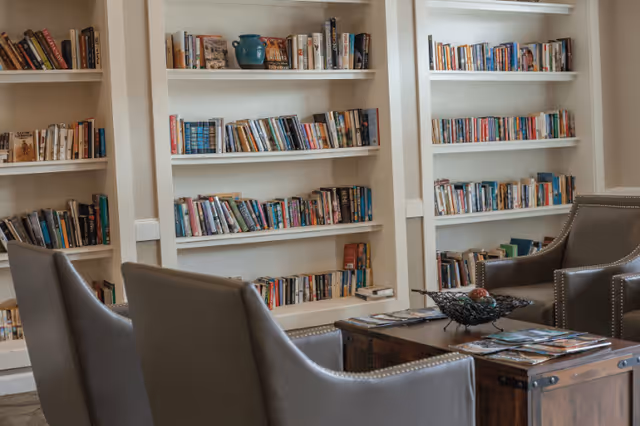 Seating area with armchairs, a wooden coffee table, and built-in bookshelves filled with books.