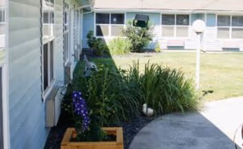 Exterior view of Homestead Place with blue siding, garden bed, and lawn.