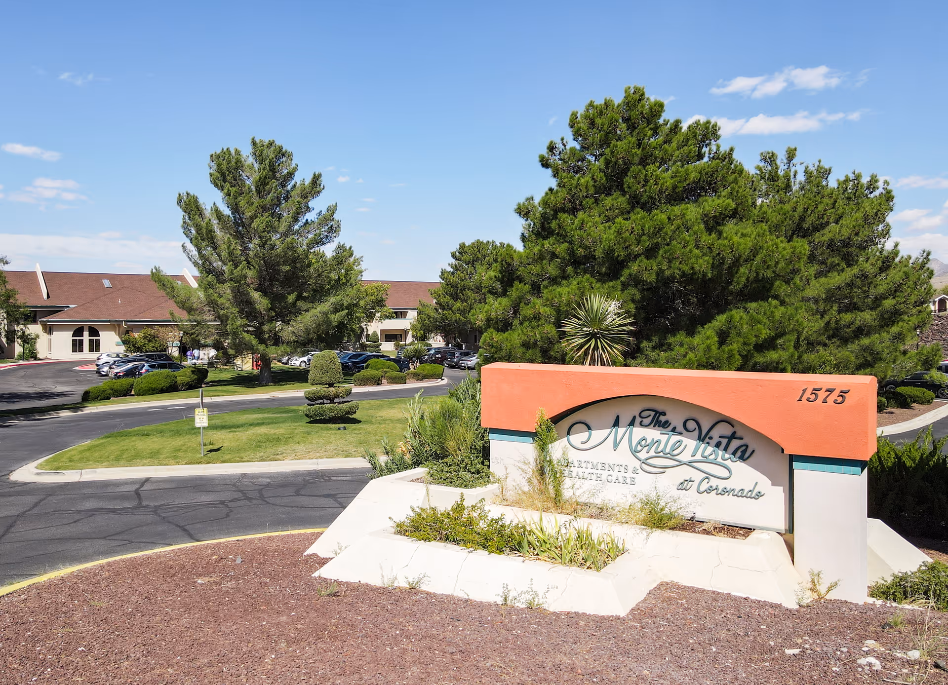 Outdoor view of The MonteVista at Coronado Assisted & Senior Living facility sign with trees, landscaping, and a parking lot in the background under a clear blue sky.
