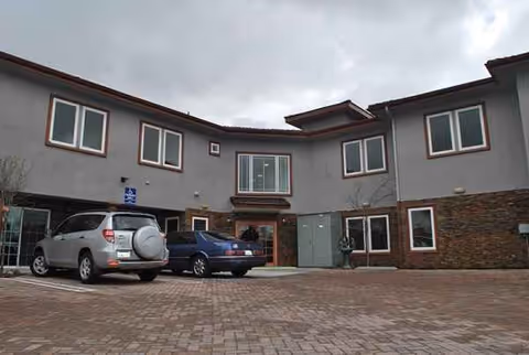 Two-story senior living facility front with parked cars and brick facade.