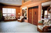 Brick-walled lobby with wicker sofas and armchairs, double wooden entry doors, and large windows.